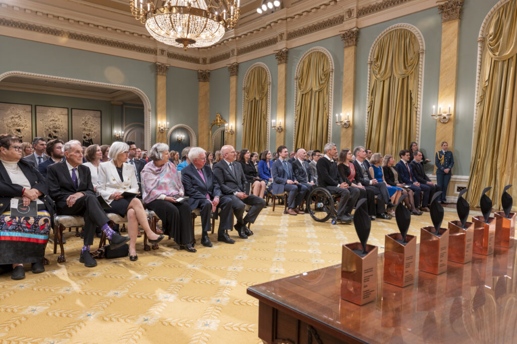 The Governor General Innovation Awards trophies in front of an engaged group of event guests at Rideau Hall